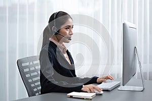 Enthusiastic asian call center with headset and microphone working on her laptop