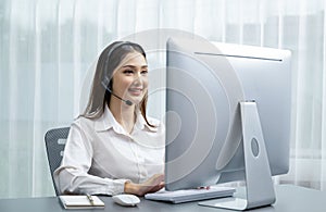 Enthusiastic asian call center with headset and microphone working on her laptop