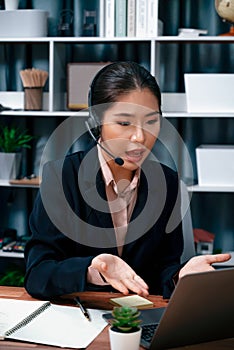 Enthusiastic asian call center with headset and microphone working on her laptop