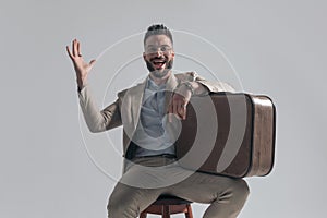 Enthusiastic bearded man holding briefcase on thigh and laughing