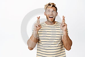 Enthusiastic blond guy makes wish with crossed fingers, looking up hopeful, wishing, yearning to achieve goal, white