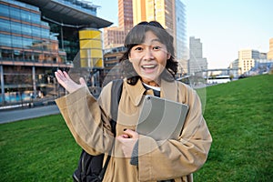 Enthusiastic brunette asian girl, student with digital tablet in her hands, looks impressed and surprised, stares at