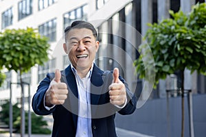 Enthusiastic businessman giving thumbs up outside corporate building