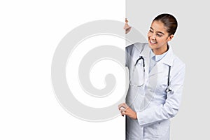 Enthusiastic Caucasian millennial doctor peering around a blank whiteboard