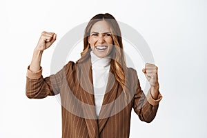 Enthusiastic corporate woman chanting, fist pump and smiling excited, encourage team, cheering and triumphing, standing