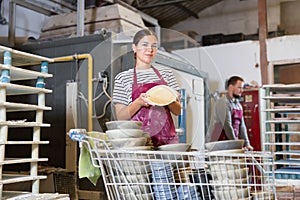 Enthusiastic female ceramicist demonstrating handcrafted plates in studio photo
