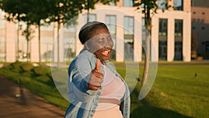 Enthusiastic happy successful African American ethnic student girl satisfied woman outdoors city showing like thumb up