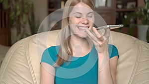 Enthusiastic happy young woman sitting in chair at home. Using her smartphone, talking with friend