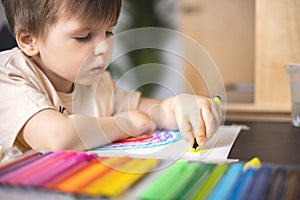 Enthusiastic male kid drawing multicolor rainbow paper sheet closeup early development art activity