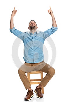 Enthusiastic man with chino pants looking up and pointing fingers in the air