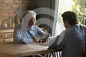 Enthusiastic old father play friendly chess match with grownup son