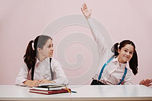 Enthusiastic perky schoolgirl raising a hand, her twin eyeing her with suspition