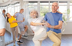 Enthusiastic senior couple practicing jive in group dance class