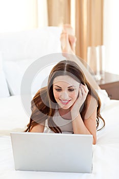 Enthusiastic woman using a laptop lying on bed