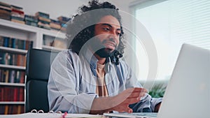 Enthusiastic young Arabian man smiling talking over headset looking in laptop