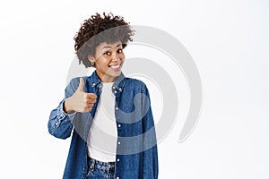 Enthusiastic young beautiful girl shows thumbs up, approves smth, recommends, smiles happy, stands over white background