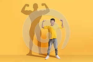 An enthusiastic young boy in a yellow shirt flexes his arms with confidence