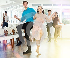 Enthusiastic young girl and guy rehearsing upbeat jive in dance studio