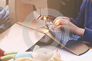 Enthusiastic young girl sews a toy dress for her doll at a compact sewing machine under supervision of her mother