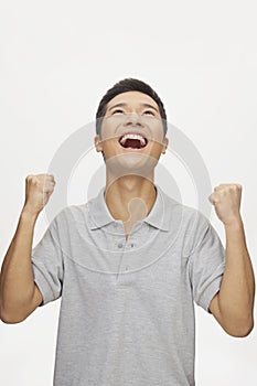 Enthusiastic young man with arms raised and looking up, studio shot