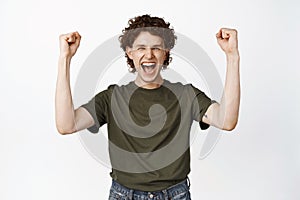 Enthusiastic young man shouting, chanting and celebrating triumph, raising hands up in victory, cheering and rooting