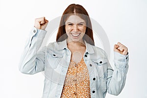 Enthusiastic young redhead girl feeling ambitious and encouraged, winning and celebrating, making fist pump gestures