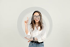 Enthusiastic young woman with glasses cheerfully pointing upwards