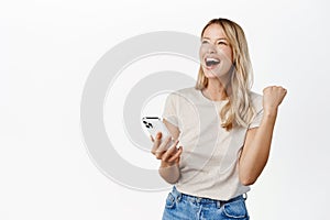 Enthusiastic young woman winning on mobile phone, rejoicing, using smartphone app, celebrating, triumphing on cellphone