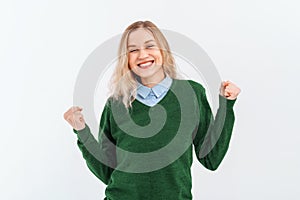 Enthusiastic young woman winning, raising fists up and celebrating, shouting with joy, wear casual clothes. Indoor studio shot on