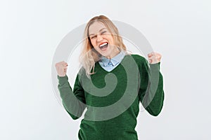 Enthusiastic young woman winning, raising fists up and celebrating, shouting with joy, wear casual clothes. Indoor studio shot on