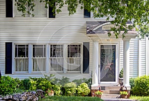 Entrance of charming white wood house with columns on porch and beautiful landscaping and overhanging branches and a red white and