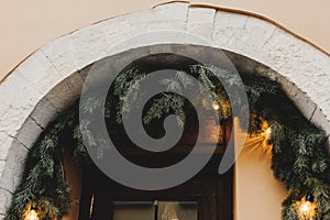 Entrance door decorated with fir branches and small lights. Christmas holiday decor