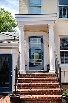 Entrance door to a large stone house with a porch and columns. Glass door, window and stone steps