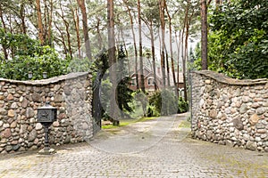 Entrance gate to a rustic, english house in the forest with stone wall and cobblestone driveway