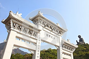 Entrance gate to Tian Tin monastery and the Big Buddha on the mountain behind at Ngong Ping village on Lantau Island, Hong Kong.