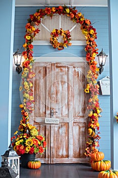 Entrance of house door decorated with autumn leaves for holiday. Fall yellow garland with leaves and pumpkins, fall decor.