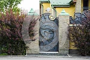 Entrance iron gate with forging elements with a stone fence decorating the house