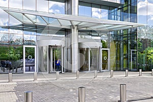 Entrance of modern office building exterior with blue sky and green trees reflections glass windows background