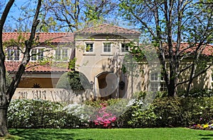 Entrance of a modern Upscale stucco house in spring with pink and white azeleas and tree leaves just starting to bud out