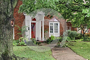 Entrance of nice brick house with bay windows after a storm that left branches and leaves littered over sidewalk and yard