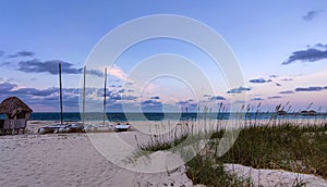 Entrance to the beach towards the ocean along a path with sailboats, boats and a hut at sunset in the evening. Tropical