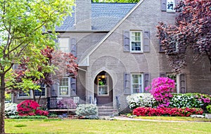 Entrance to grey brick two story house landscaped with Japanese Maples and Azaleas with shutters and a front seating area