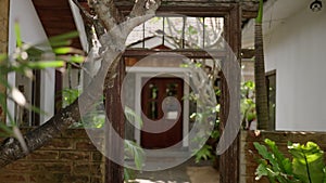 Entrance to hipster cafe with wooden gate, big green exotic plants outside on Bali. Tropical restaurant on sunny day