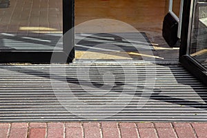 Entrance to the hotel from a plink on a foot mat through a glass door.