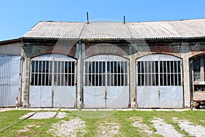 Entrance to large old train station repair workshop with overgrown train tracks leading to front doors