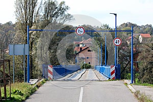 Entrance to partially renovated wavey old wooden bridge with new blue metal frame on each side and strong support with LED street