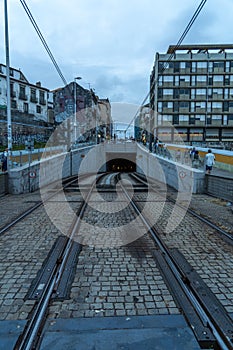 Entrance to the Porto metro tunnel or tramway in perspective of the Dom Luis bridge at sunset, under a cloudy sky and tourists