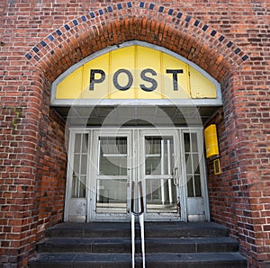 Entrance to the Post office in an historic building with a yellow sign, an old door and an arch of brick architecture in the old