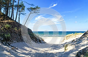 Entrance to a sandy beach through dunes, Baltic Sea near Åeba, Poland, Europe. Summer, little waves on the water, blue sky.