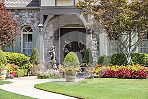 Entrance to upscale rock house with beautiful landscaping and a statue and wreaths and benches beside front porch